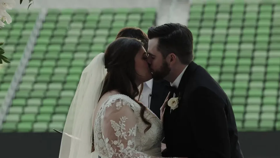 Gabby and Nic kiss in front of the green seats at Q2 Stadium in Austin, a still from Adam Grumbo's finalist wedding film