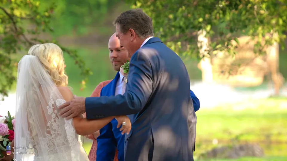 The father of the bride hands the bride to the groom under the trees at the Venue at Waterstone, a still from Adam Grumbo's film of the day